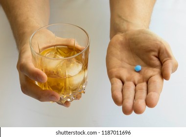 Close-up Male Hand Holding Pill For Sexual Impotence And Glass With Whiskey. Medication. Viagra Generic Blue Pill And Drink. White Background. Heart Attack Or Diseases.