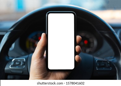 Close-up of male hand holding smartphone with white mockup on screen, background of car steering wheel. - Shutterstock ID 1578041602