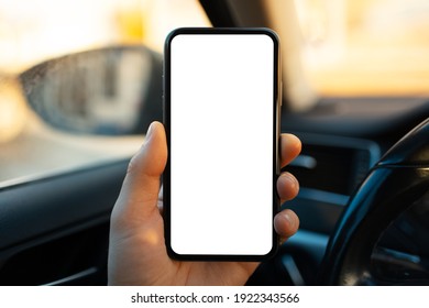 Close-up of male hand holding smartphone with white mockup on screen against blurred background of car interior.