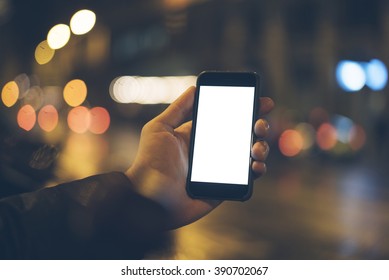 Closeup Of Male Hand Holding And Using Modern Smart Phone With Blank Screen For Your Text Or Content, With Night Light Bokeh