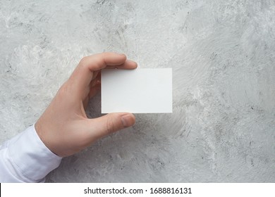 Closeup Of Male Hand Holding White Business Card On Concrete Wal