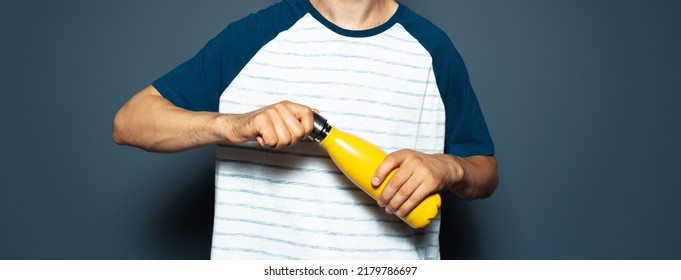 Close-up Of Male Hand Holding Yellow Metal Water Bottle On Blue. Panoramic Banner.