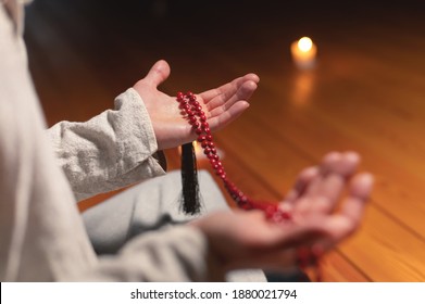 close-up the male hand of a monk practicing meditation holds a red rosary in a dark room by candlelight. Practice and enlightenment