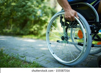 Close-up of male hand on wheel of wheelchair during walk in park