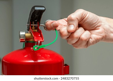 Closeup of a male hand pulling the safety pin of a manual chemical fire extinguisher. - Powered by Shutterstock