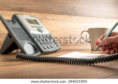 Closeup of male hand taking important notes as he answers a call on a classical landline telephone. Concept of assistance and secretary work.