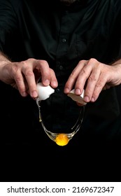 Closeup Of Male Hands Cracking Egg For Natural Protein Shake Eggnog. Baker Man Wearing A Black Outfit In Darkness. Eggshell, Egg White, Yolk.