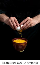 Closeup Of Male Hands Cracking Egg For Natural Protein Shake. Baker Man Wearing A Black Outfit In Darkness. Eggshell, Egg White, Yolk.