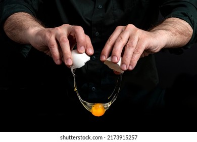 Closeup Of Male Hands Cracking Egg For Natural Protein Shake. Baker Man Wearing A Black Outfit In Darkness. Eggshell, Egg White, Yolk.