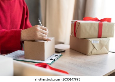 close-up of male hands filling out a mailing form on a parcel box in the office or at home. small business owner preparing to send christmas presents. postal delivery and people. shipment concept.