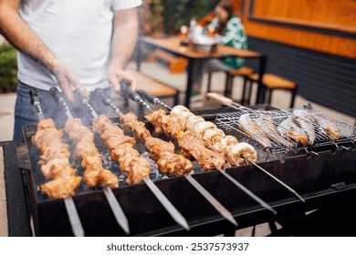 Close-up of male hands holding skewers with meat, mushrooms and grilled fish. Man cooks delicious pieces of meat baked on coals. Fresh barbecue on outdoor campfire. Festive lunch in backyard of house - Powered by Shutterstock