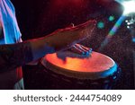 Close-up of male hands, musician playing bongo drums on dark background with stage lights. African culture live event. Concept of music, instruments, concert, sound, equipment, festival
