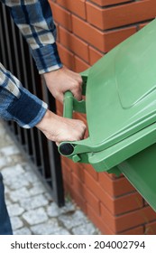 Close-up of a male hands pushing a wheeled dumpster