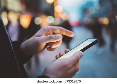 Nahaufnahme männlicher Hände, die eine SMS-Nachricht über Smartphone im Freien tippen, Hipster-Mann genießt abends spazieren und mit seinem Handy, Bokeh-Leuchten