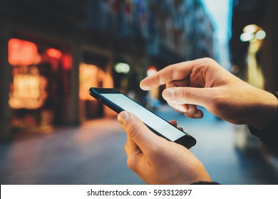 Nahaufnahme männlicher Hände mit Smartphone mit leerem Bildschirm mit Kopienraum für Design- oder Textnachrichten, junger Mann, der eine SMS-Nachricht in sozialen Netzwerken im Freien schreibt, abendliche Straßen im Hintergrund