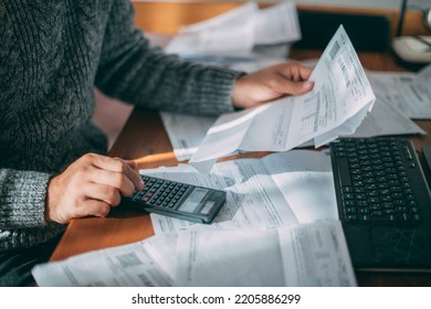 Close-up of male hands with a utility bill, a lot of checks and a calculator on the table. The man considers the costs of gas, electricity, heating. The concept of increasing tariffs for services