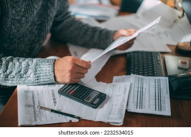 Close-up of male hands with a utility bill, a lot of checks and a calculator on the table. The man considers the costs of gas, electricity, heating. The concept of increasing tariffs for services - Shutterstock ID 2232534015