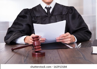 Close-up Of Male Judge In Front Of Mallet Holding Documents