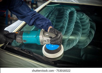 Close-up of a male mechanic with a blue prism and protective gloves polishes the front glass of the car with a polishing machine from small scratches