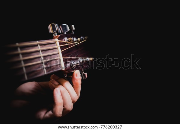 closeup male musician hands tuning acoustic guitar\
strings, isolated on\
black