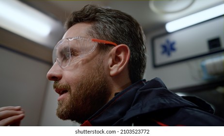 Closeup Male Paramedic Discussing Job With Colleague In Ambulance Car. Portrait Of Ambulance Doctor With Shocked Face Expression. Angry Medical Worker Talking With Coworker At Night Shift