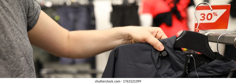 Close-up Of Male Person Choosing Black Casual Jacket In Shopping Centre. Red Discount On Top Clothes. Low Price. Stylish Purchase In Mens Department. Store Concept