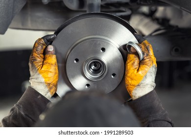 Closeup male tehnician mechanic greasy hands in gloves install new car oem brake steel rotor disk during service at automotive workshop auto center. Vehicle safety checkup and maintenance concpet