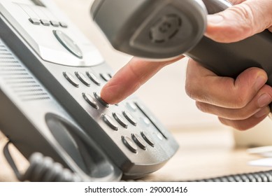 Closeup of male telemarketing salesperson holding a telephone receiver dialing phone number to make a business call.
