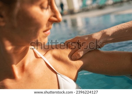 Close-up of a male trainer's hand on a female client's shoulder during a pool rehabilitation session