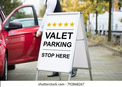 Close-up Of Male Valet Standing Near Valet Parking Sign