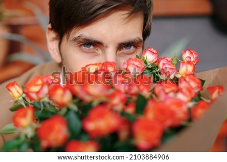 Close-up man blue eyes looking to camera through a bouquet of flowers, bunch of roses. Gorgeous red yellow roses.