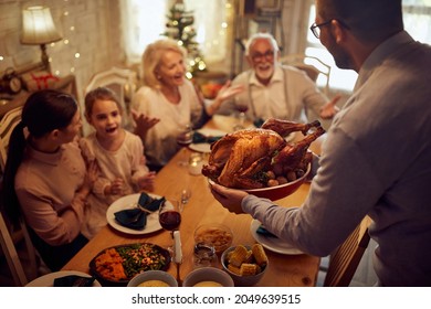 Close-up of man brining roast turkey at dining table while celebrating Thanksgiving with his family at home. - Powered by Shutterstock