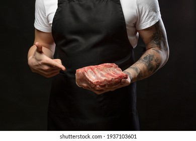 Closeup A Man Butcher Wearing Black Apron Pointing Finger To Raw Pork Rib. Mockup, Place For Text.