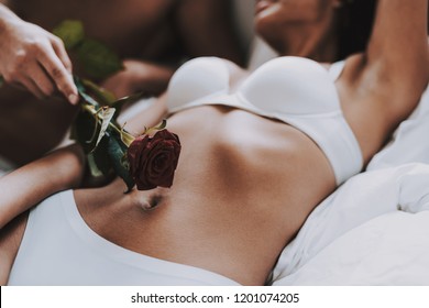 Closeup of Man Caresses Beautiful Woman using Rose. Young Beautiful Couple in Underwear Lying on Bed. Passionate Romantic Lovers about to have Sex at Home. Passion, Intimate Relationship and Love