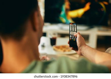 Close-up of man changing channels while watching TV at home. 