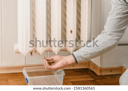 Closeup of man checking leaks in old cast iron battery at home. Water leaking from an old cast iron radiator, showing damage and the need for heating system maintenance