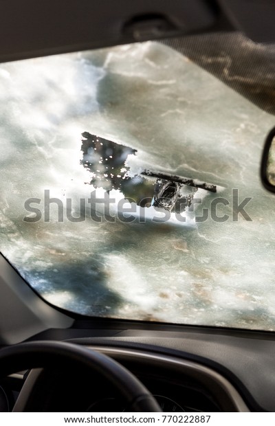 Close-up of man cleaning car window from snow and\
ice. Scraping ice from a windshield has been taken from the inside\
of the car. Transportation winter driving weather people and\
vehicle concept