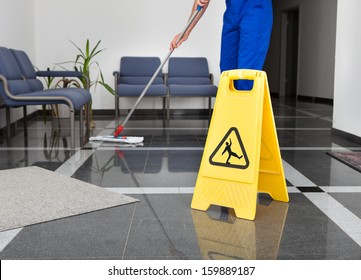 Close-up Of Man Cleaning The Floor With Yellow Wet Floor Sign