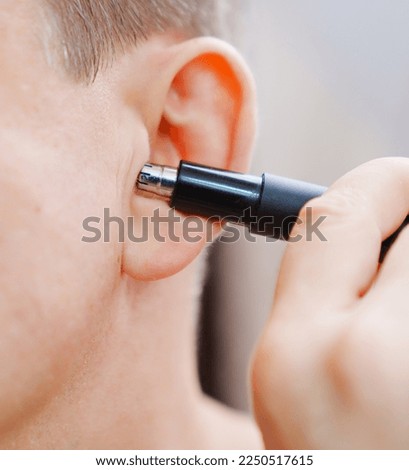 close-up. a man cuts his ear hair with a trimmer. the concept of personal hygiene and removal of excess hair.
