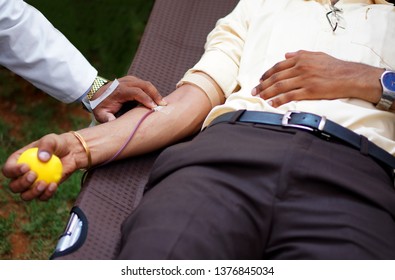 Closeup Of A Man Donating Blood, In A Camp,sleeping On Cot And Holding Rubber Ball To Squeeze                                