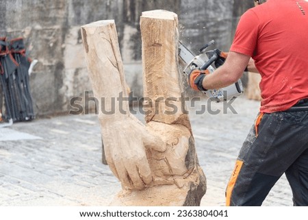 Close-up of a man dressed in work clothes making a wooden sculpture by carving a log with a chainsaw