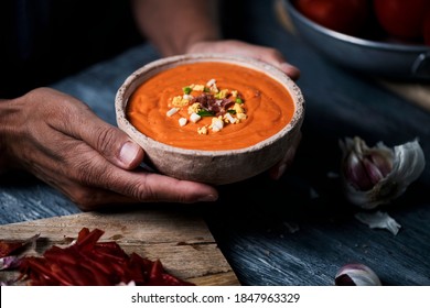 closeup of a man with an earthenware bowl in his hands with fresh made spanish salmorejo cordobes or porra antequerana, a cold tomato soup topped with serrano ham, boiled egg and green pepper