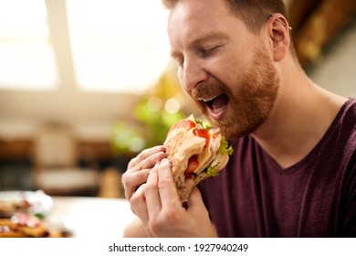 Close-up of man eating sandwich with eyes closed at home. 