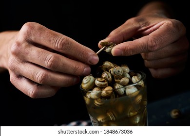 Closeup Of A Man Eating Some Caracolillos En Caldo, A Spanish Recipe Of Small Snails Cooked And Served In Broth Typical Of Andalusia, Using A Toothpick