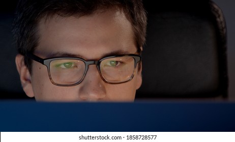 Closeup Of Man Eyes In Eyeglasses In Front Of The Computer In Home Office, Concentrated Look. Young Man Sitting At Home Working Alone At Night