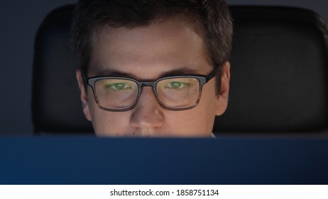 Closeup Of Man Eyes In Eyeglasses In Front Of The Computer In Home Office On Background Of Grey Wall. Young Man Sitting At Home Working Alone At Night