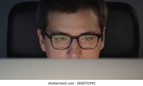 Closeup Of Man Eyes In Eyeglasses In Front Of The Computer In Home Office On Background Of Grey Wall. Young Man Sitting At Home Working Alone At Night