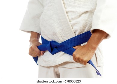 Close-up Of A Man Fighter In A White Kimono For Judo, Jiu Jitsu Ties Up A Blue Belt On An Isolated White Background