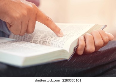 Closeup of Man finger pointing text in a bible. Man reading a bible or book with sunlight. - Powered by Shutterstock