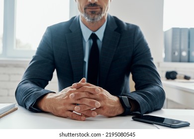 Close-up of man in formalwear keeping hands clasped while sitting at the desk in office
